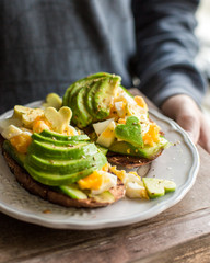 Whole grain toasts with avocado, egg, cucumber. A useful delicious breakfast. Heart from avocado. Atmospheric photo with hands Place for text, top view
