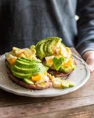 Whole grain toasts with avocado, egg, cucumber. A useful delicious breakfast. Heart from avocado. Atmospheric photo with hands Place for text, top view
