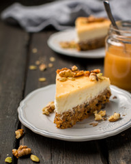 Carrot nut vanilla cheesecake with salty homemade caramel on a white plate on a dark wooden vintage background. Two pieces of homemade cheesecake. Caramel sauce in a jar.