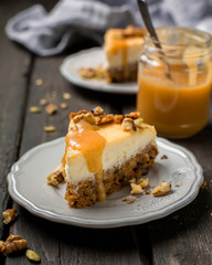 Carrot nut vanilla cheesecake with salty homemade caramel on a white plate on a dark wooden vintage background. Two pieces of homemade cheesecake. Caramel sauce in a jar.