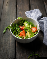 Useful tasty salad with arugula, fresh strawberries and avocado, seasoned with honey, wine vinegar, olive oil and poppy seeds on a vintage dark vintage background.