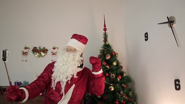 Santa Claus takes pictures of himself. In the room near the Christmas tree, Santa Claus is holding a self-stick and taking pictures of himself in different ways.