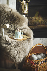 Cup of hot chocolate on chair and basket with balls of yarn