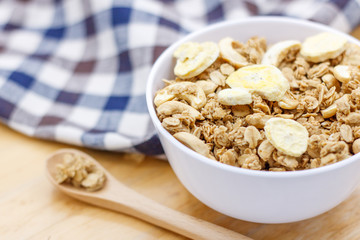 Healthy breakfast, granola with nuts and dry bananas in white blow on wooden table with wooden spoon and cute fabric.