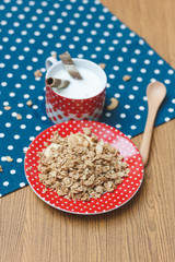 Plate of granola with cup of milk on polka on a wooden table. Healthy food concept.