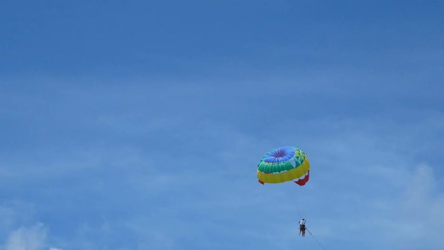4K. excited tourists hanging on parasailing flying high in the sky, outdoor extreme sport summer activity. colorful parachute on blue sky background