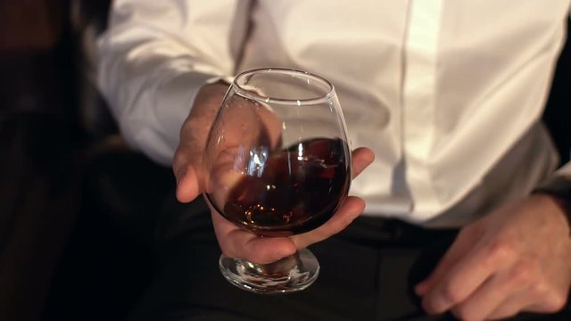 Swirling brandy in glass, slow motion. Man keeping a glass of cognac, close-up.