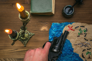 Treasure map on wooden table. Treasure hunt. Adventurer man holding in hands handgun and showing...