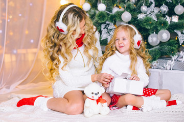 Obraz na płótnie Canvas Happy female model with long blond hair and her adorable little girl have fun together to celebrate Christmas, unwrap presents, have a smiling expression, joy.