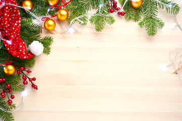 Christmas background decoration with lights, balls, santa hat and fir tree branches flat lay on wooden texture. Top view with blank space.