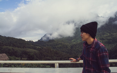 Asian young man in Scottish shirt and black hat hiking at mountain peak above clouds and fog Hiker outdoor. Doi Luang Chiang Dao Chiangmai Province,In morning.