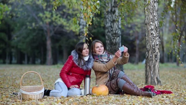 two young women in autumn Park photographed on the phone