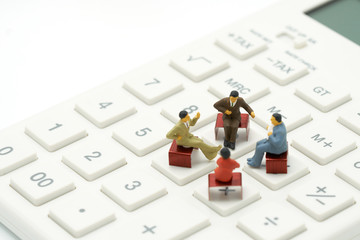 Miniature 4 people sitting on red staples placed on a white calculator. meeting or Discussion as...