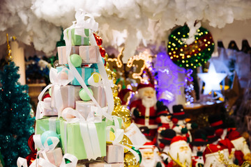 Pile of gift boxes decorated in Christmas tree with santa claus and Christmas ornament decorations in the background