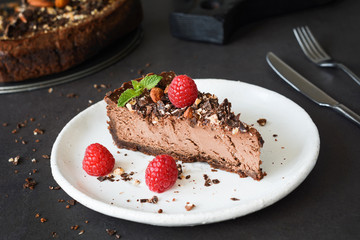 Chocolate cheesecake with raspberries, nuts and mint leaf on white plate. Closeup view, selective focus