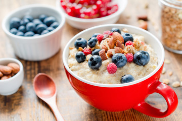 Oatmeal porridge bowl with blueberries, nuts and raspberries. Jar of granola on side. Healthy colorful breakfast for kids. Closeup view, selective focus