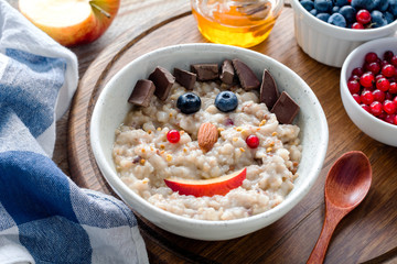 Colorful and healthy breakfast for kids: oatmeal porridge with berries, nuts and organic chocolate with a funny face. Meal for kids