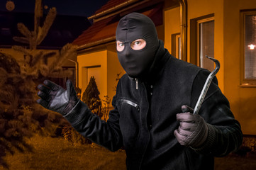 Masked thief in balaclava with crowbar wants to rob a house