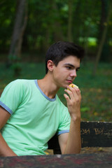 An imaginary teenager sits on a bench in nature. He eats an apple