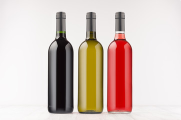 Three wine bottles  different colors  on white wooden board, mock up. Template for advertising, design, branding identity.