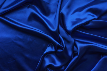 Blue satin, silky fabric, wave, draperies. Beautiful textile backdrop. Close-up. Top view 