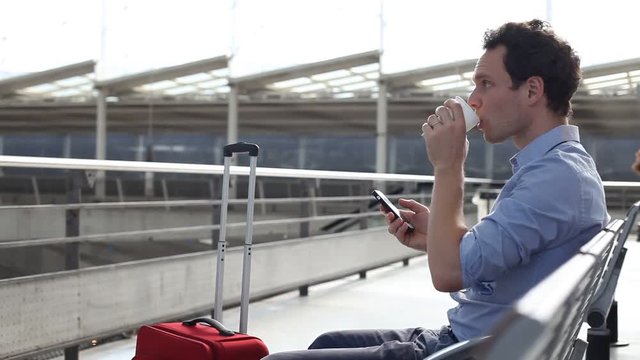young man drinking coffee in the airport and reading email on smart phone via wifi internet connection