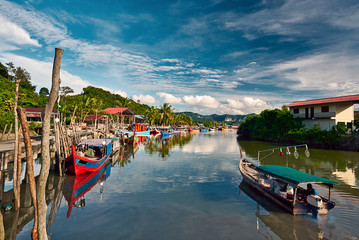 A local fisherman goes out on a boat from boats park to the sea for fishing. Traditional colorful asian fishing boats in fishing village. Langkawi island, Malaysia. - obrazy, fototapety, plakaty