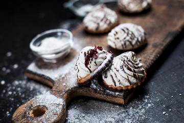 small chocolate cakes with different stuffings, sprinkled with chocolate topping, sprinkled with powdered sugar on a wooden board on a dark background