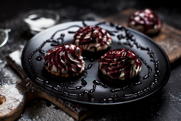 small desserts with different stuffings, sprinkled with berry topping, sprinkled with powdered sugar on a black plate on a wooden board on a dark backgroun