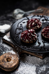 small desserts with different stuffings, sprinkled with berry topping, sprinkled with powdered sugar on a black plate on a wooden board on a dark backgroun