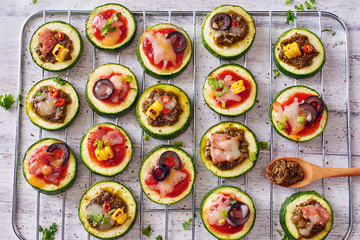 Top view oh healthy zucchini mini pizza. Squash circles with tomato and pesto sauce, cheese, corn, olive and bacon on white table. 