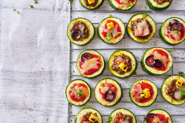 Top view oh healthy zucchini snack with copy space. Baked zucchini circles with tomato and pesto sauce, cheese, corn, olive and bacon on white table. 