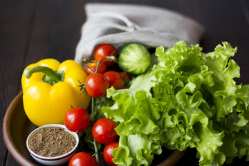 fresh organic vegetables: tomatoes, peppers, cucumber, chili, spices and salad in a clay plate on the table dark wood