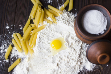 broken egg on flour, pasta and spices on a wooden table