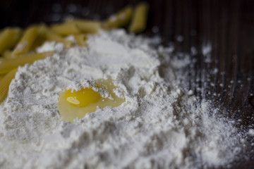 broken egg on flour and pasta on wooden table