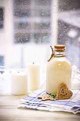 New Year's still life with a bottle of milk, biscuits, white candles, tablecloth in a box on a white wooden table, a country background in a clear sunny day