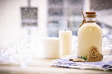 New Year's still life with a bottle of milk, biscuits, white candles, tablecloth in a box on a white wooden table, a country background in a clear sunny day