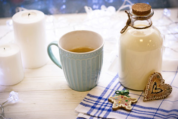 New Year's still-life with a bottle of milk, blue cup of coffee, biscuits, white candles, tablecloth in a box on a white wooden table, bright background on a sunny day