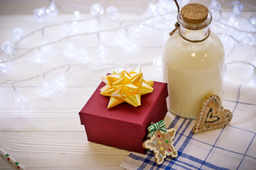 On the wooden table there is a bottle of milk and a gift in a red box, two cookies in the form of a star and a heart