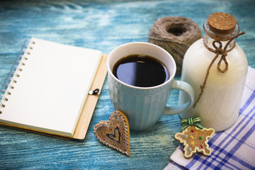Festive still life with a bottle of milk, a cup of freshly brewed fragrant coffee, biscuits, a skein of yarn, a notepad, a checkered tablecloth on a turquoise wooden table, a light background