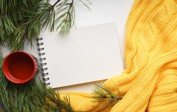 Christmas background with a Cup  of tea, a notebook, branches of pine with large needles and a yellow sweater. Top view close-up