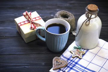 Festive still life with a bottle of milk, a cup of freshly brewed fragrant coffee, biscuits, a skein of yarn, a gift box, a checkered tablecloth on a gray wooden table, a dark background