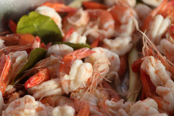 Pile of steamed shrimp in white and red color with green lime leaf. It is a small free swimming crustacean with an elongated body, typically marine and frequently harvested for food.