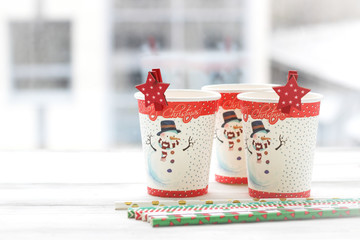 Festive still life with three glasses with a picture of a snowman on a white wooden table, multicolored sticks, a country background on a sunny day