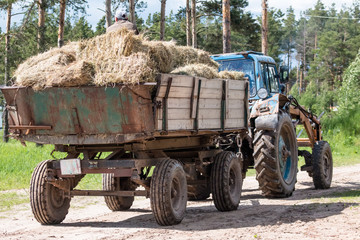 A large tractor carries bale with hay along the picturesque forest road