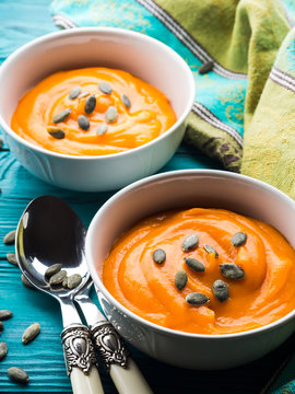 Creamy pumpkin soup in white bowls on green wooden table