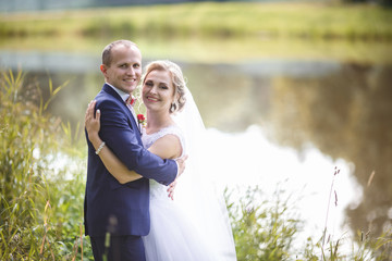 The bride and groom in nature near the lake. Bride is hugging the groom. Wedding day. The best day of a young couple.