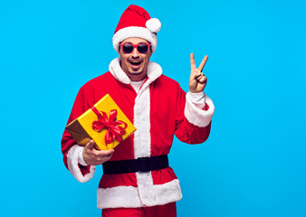 Fototapeta na wymiar Santa Claus. Young Santa Man with Christmas Gift Boxes Presents Having Fun Smiling. Handsome Fashion guy Happy. New Year. Emotional Sporty Santa Claus, Sunglasses. Colorful Xmas Holiday
