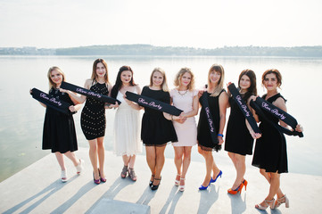 Fototapeta premium Group of 8 girls wear on black and 2 brides at hen party against sunny beach.