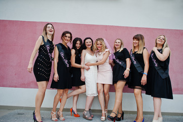 Fototapeta premium Group of 8 girls wear on black and 2 brides at hen party posed against pink wall.